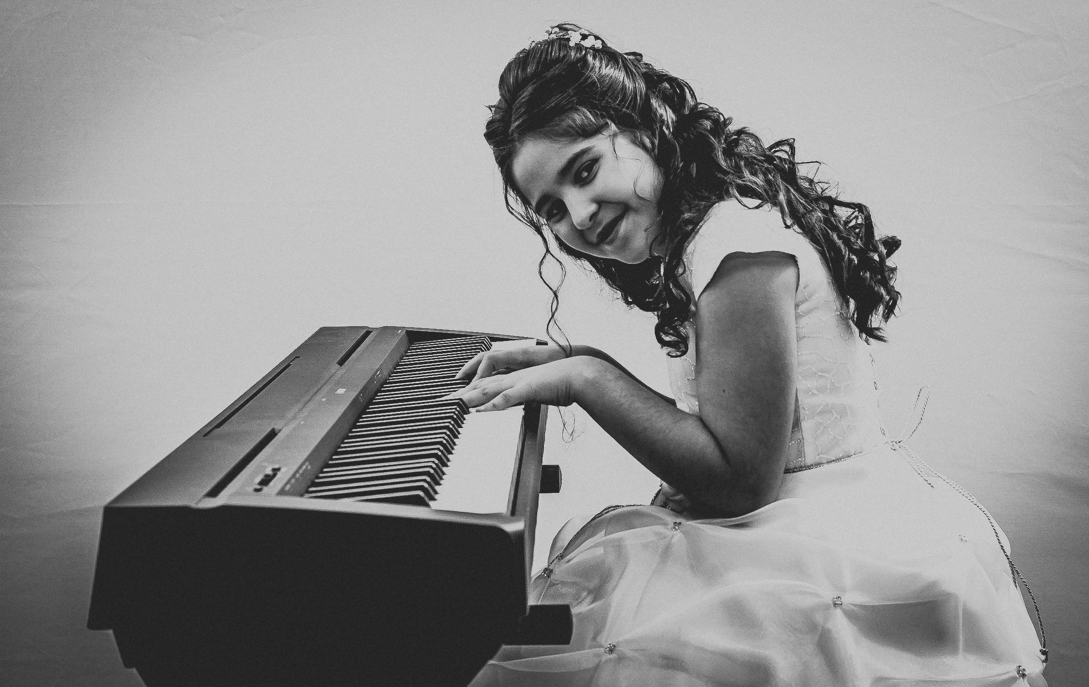 Jeune fille en robe de première communion jouant du piano, regard vers l’objectif