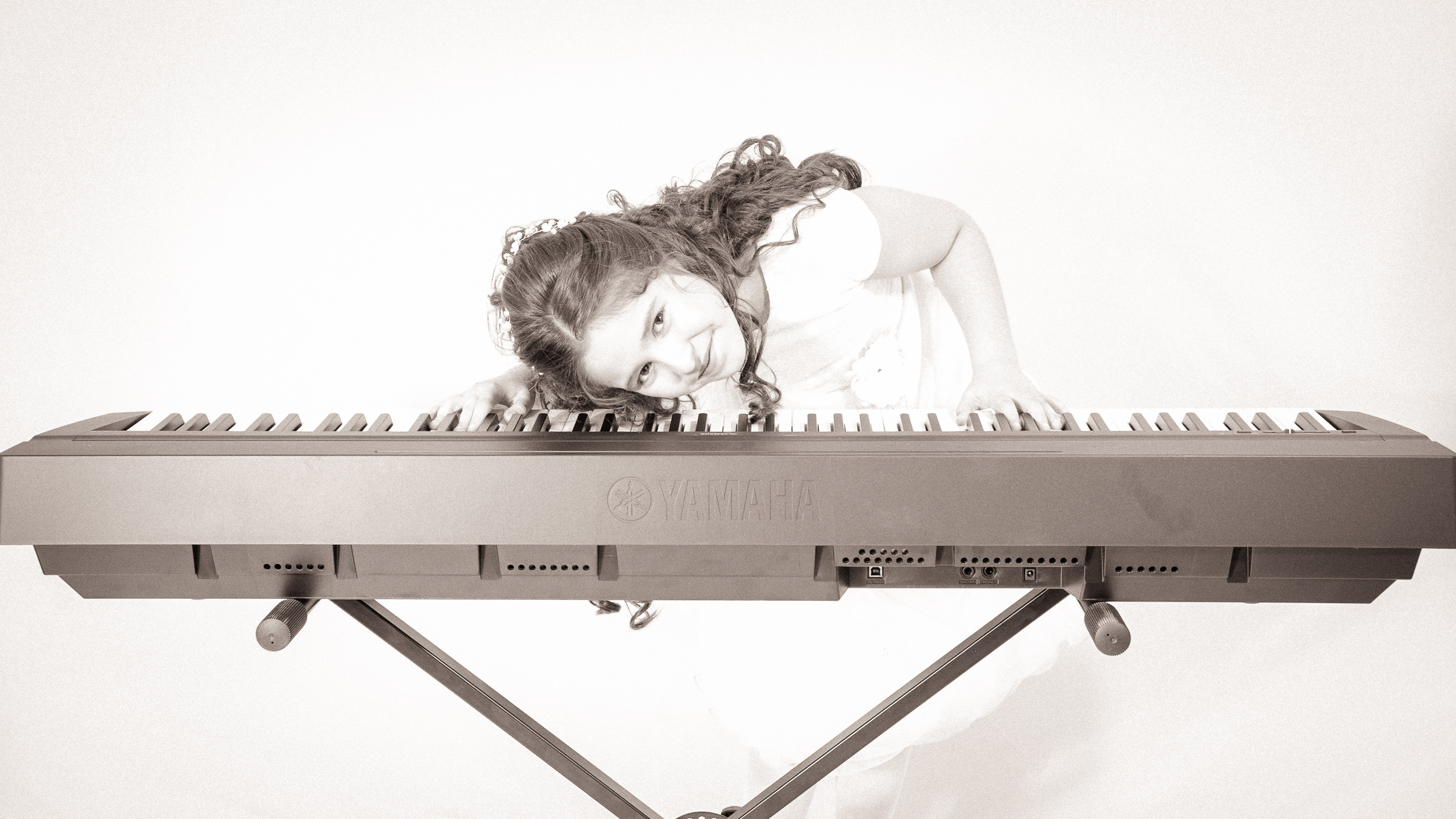 Jeune fille en robe de première communion penchée au-dessus du clavier du piano