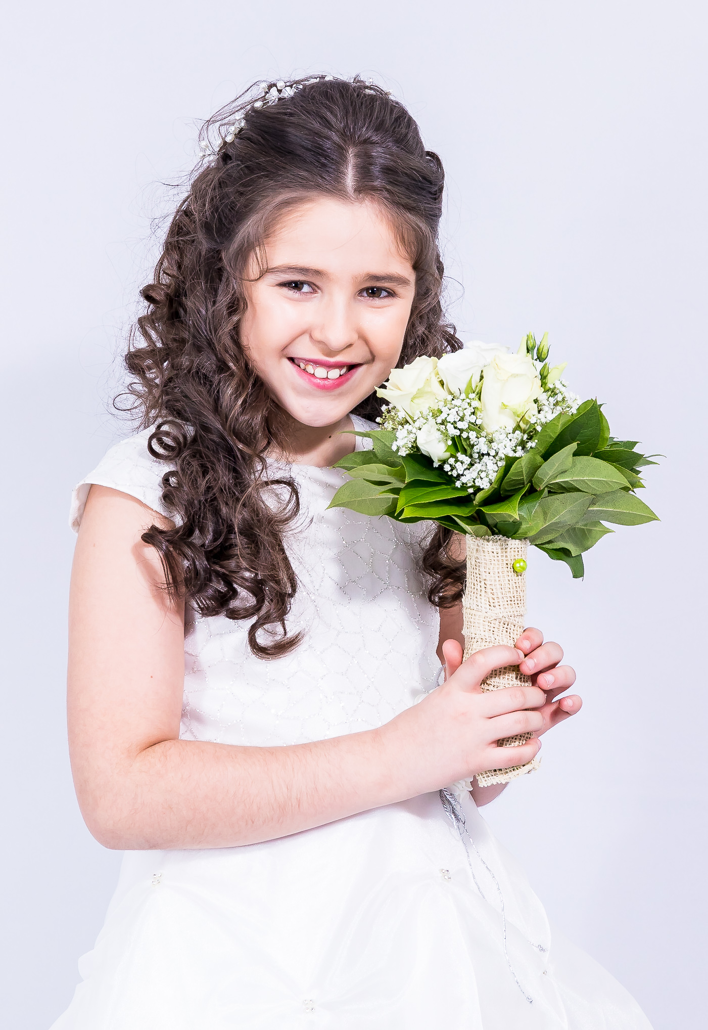 Jeune fille en robe de première communion tenant un bouquet de roses blanches, sourire
