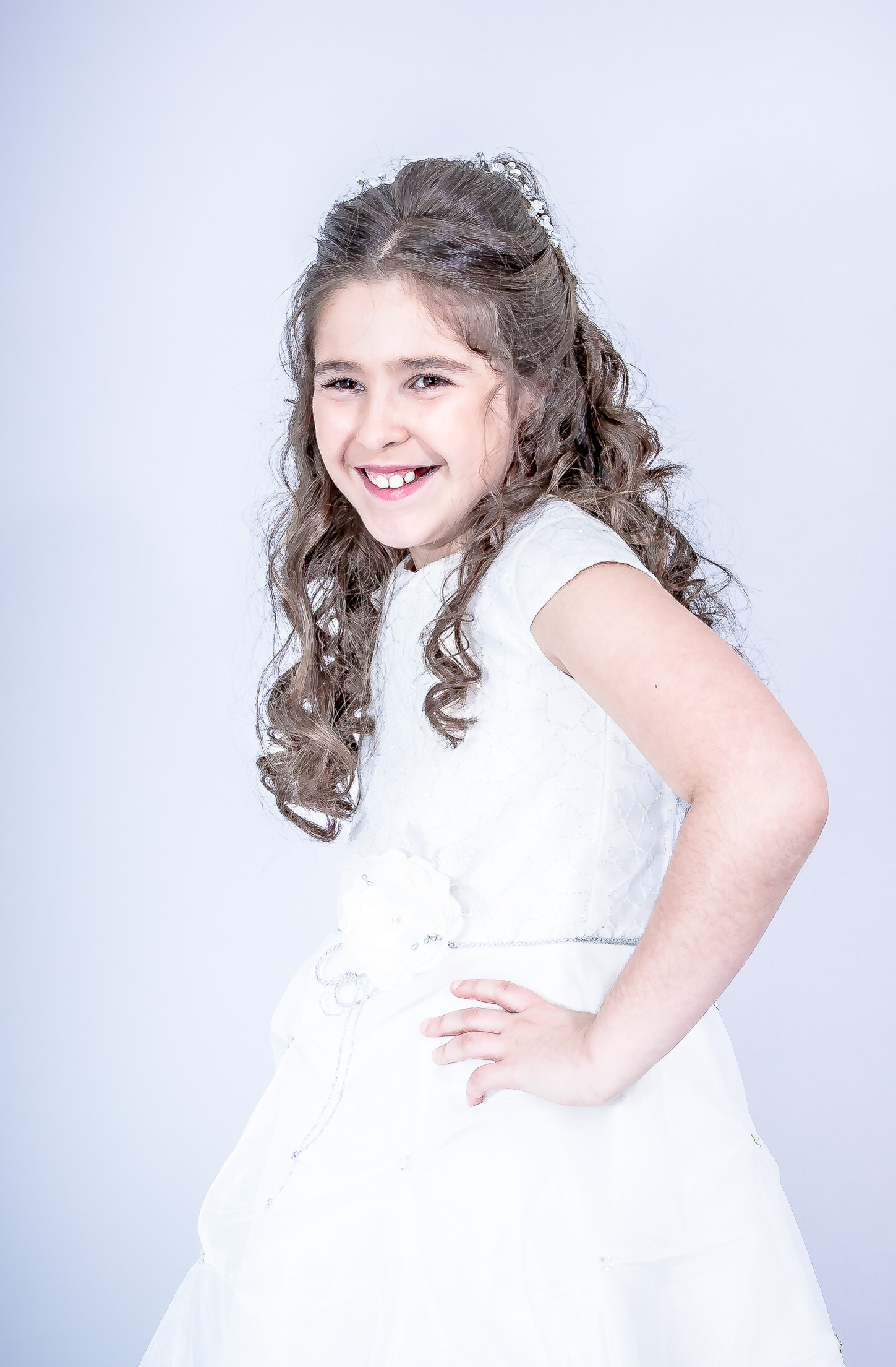 Jeune fille en robe de première communion, main sur la hanche, sourire joyeux