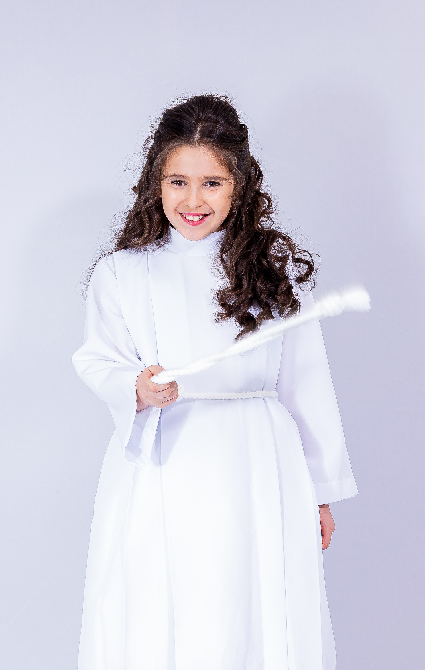 Jeune fille en aube blanche de communion, tenant un cierge, sourire