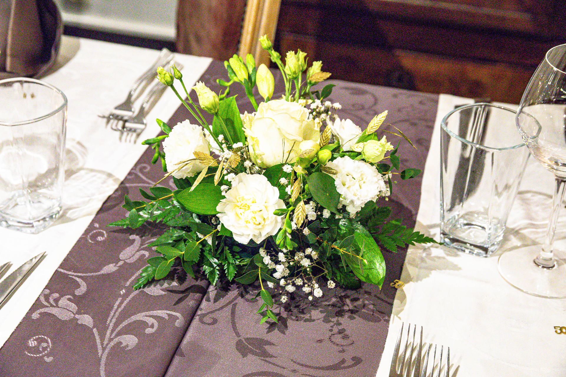 Composition florale blanche sur nappe grise, verres et couverts