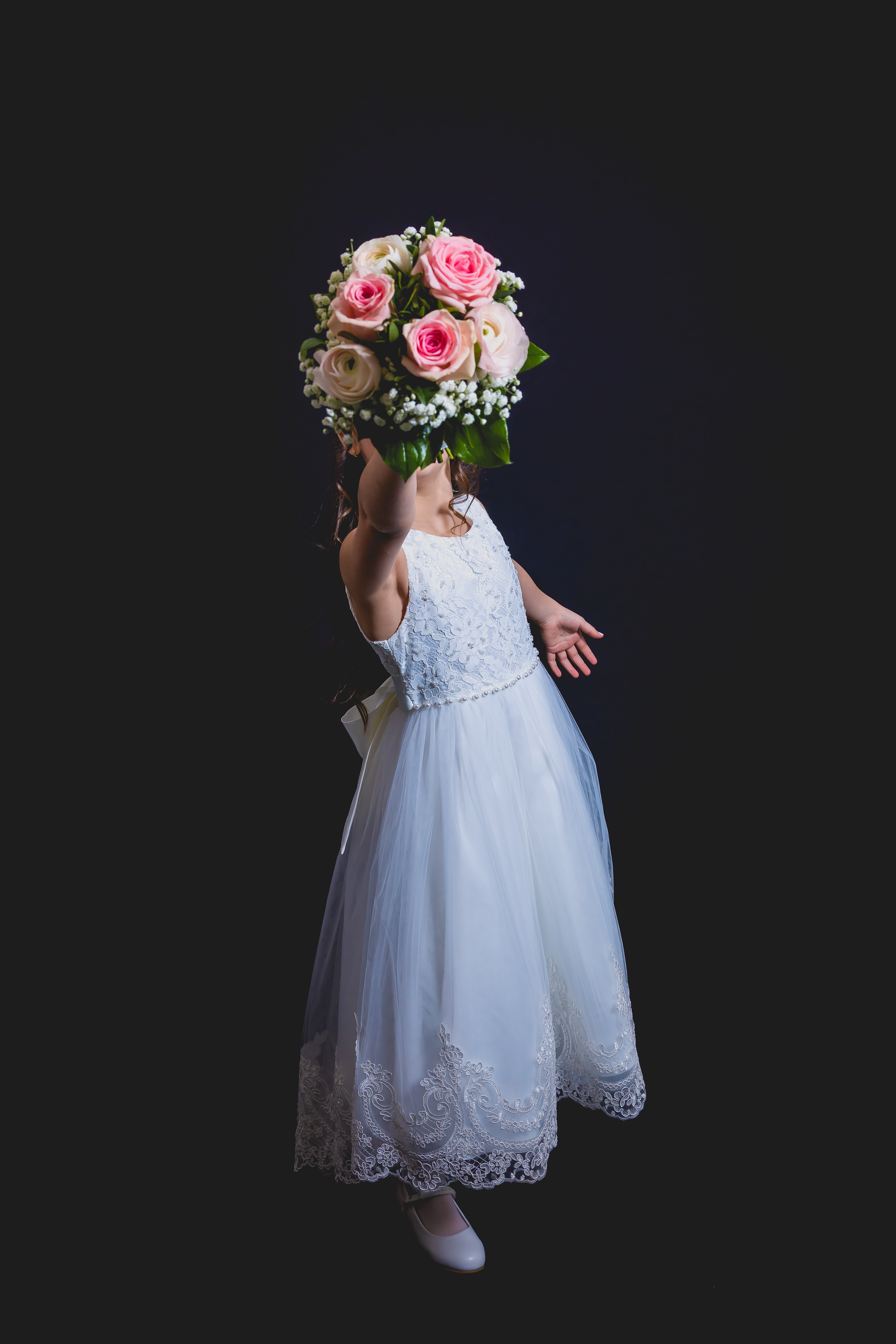 Jeune fille en robe de communion, bouquet de roses roses levé masquant le visage
