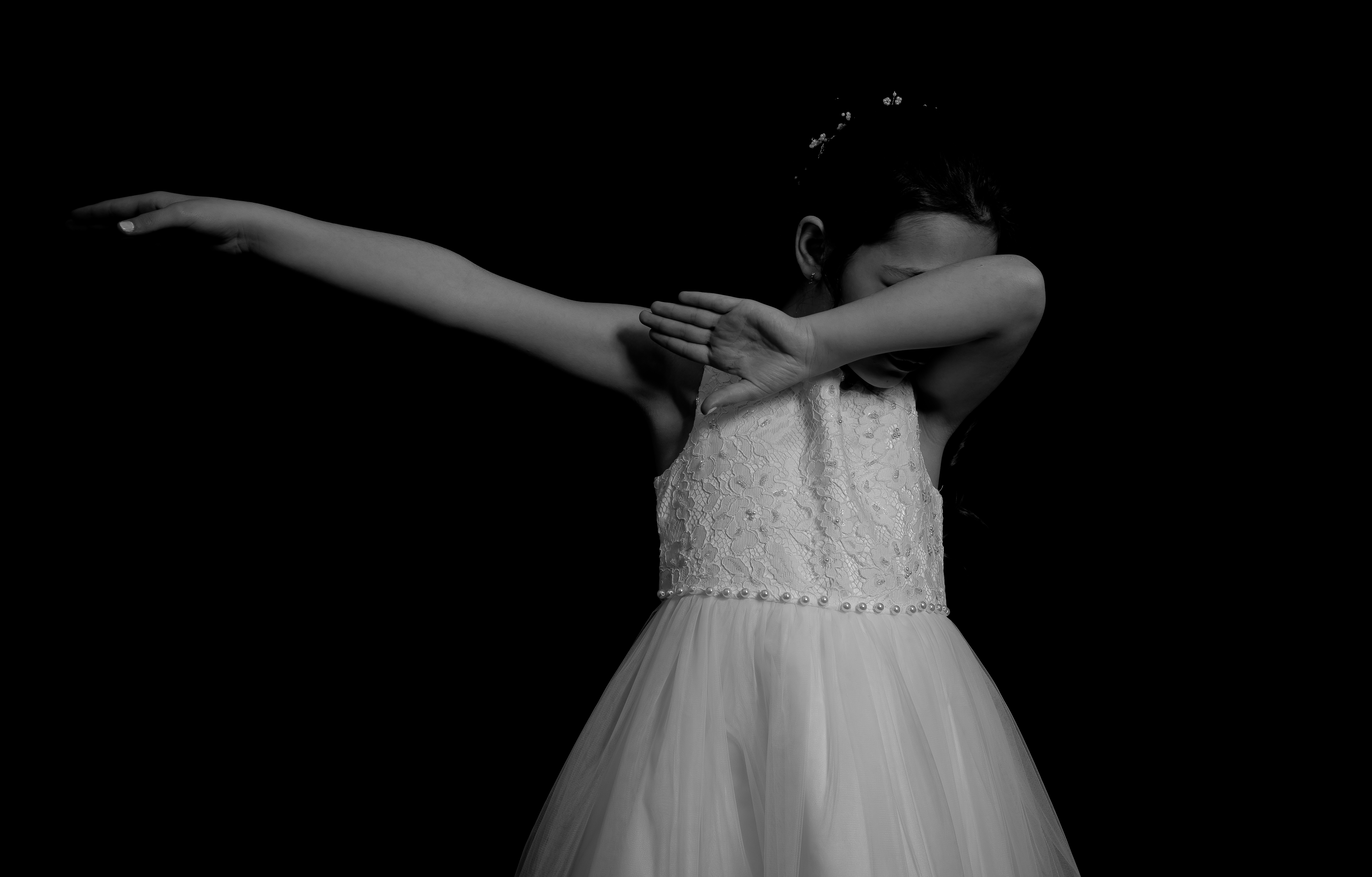 Jeune fille en robe de communion, bras tendu façon danse, vue de dos en noir et blanc