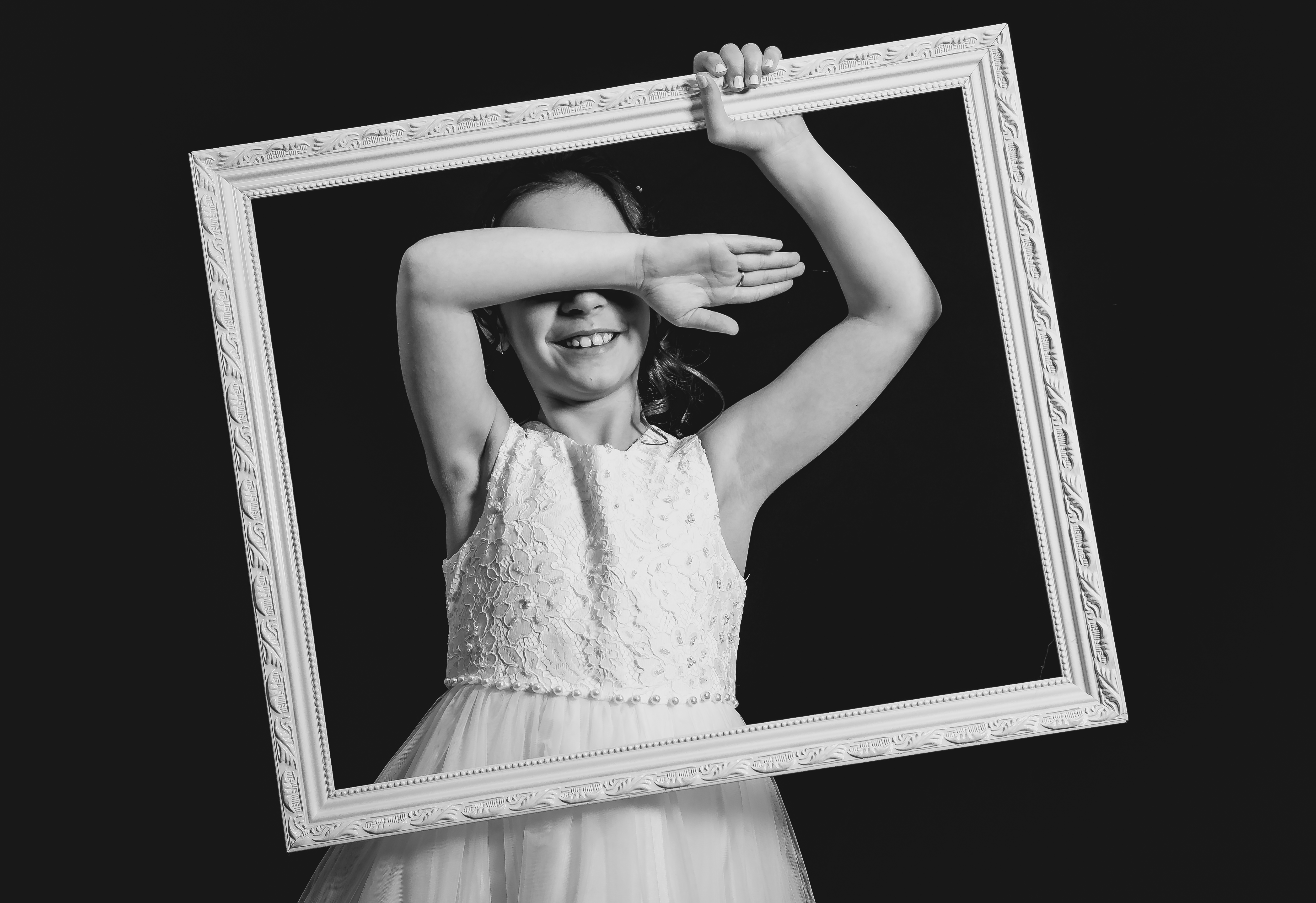 Jeune fille tenant un cadre vide devant son visage, bras levé, sourire, noir et blanc
